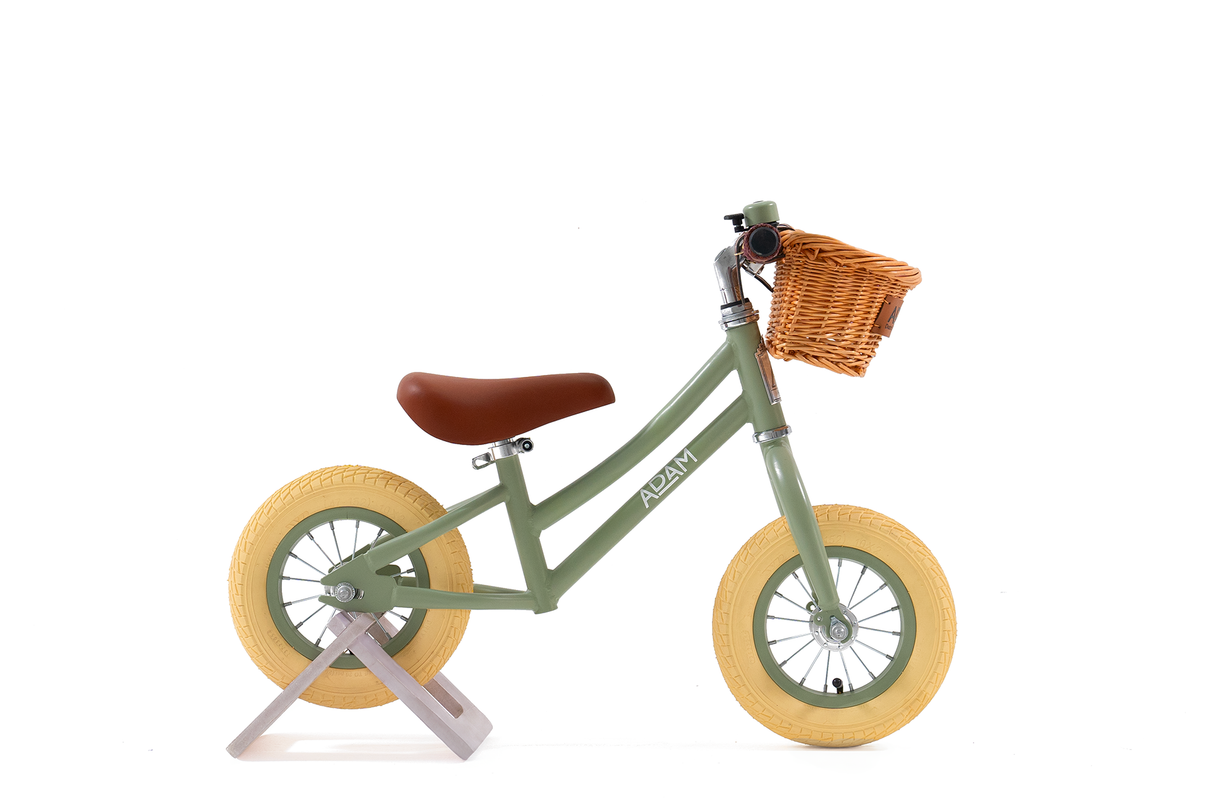 Green balance bike with a brown basket on a white background