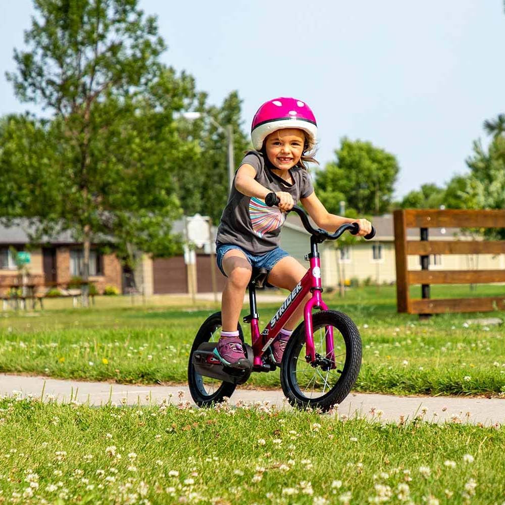 Child riding a pink balance bike with a helmet in a park setting