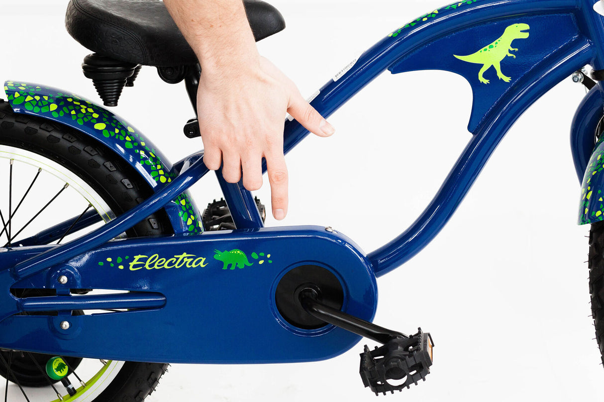Blue children's bike with dinosaur graphics and a hand on the pedal, brand 'Electra' visible.