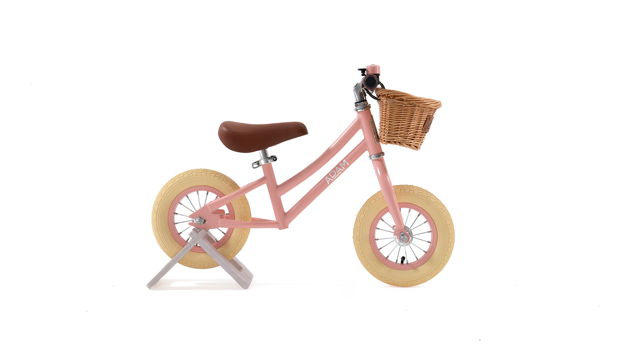 Pink balance bike with a wicker basket on a white background