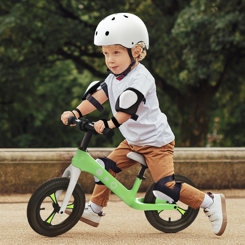 Child riding a green balance bike outdoors with a blurred natural background