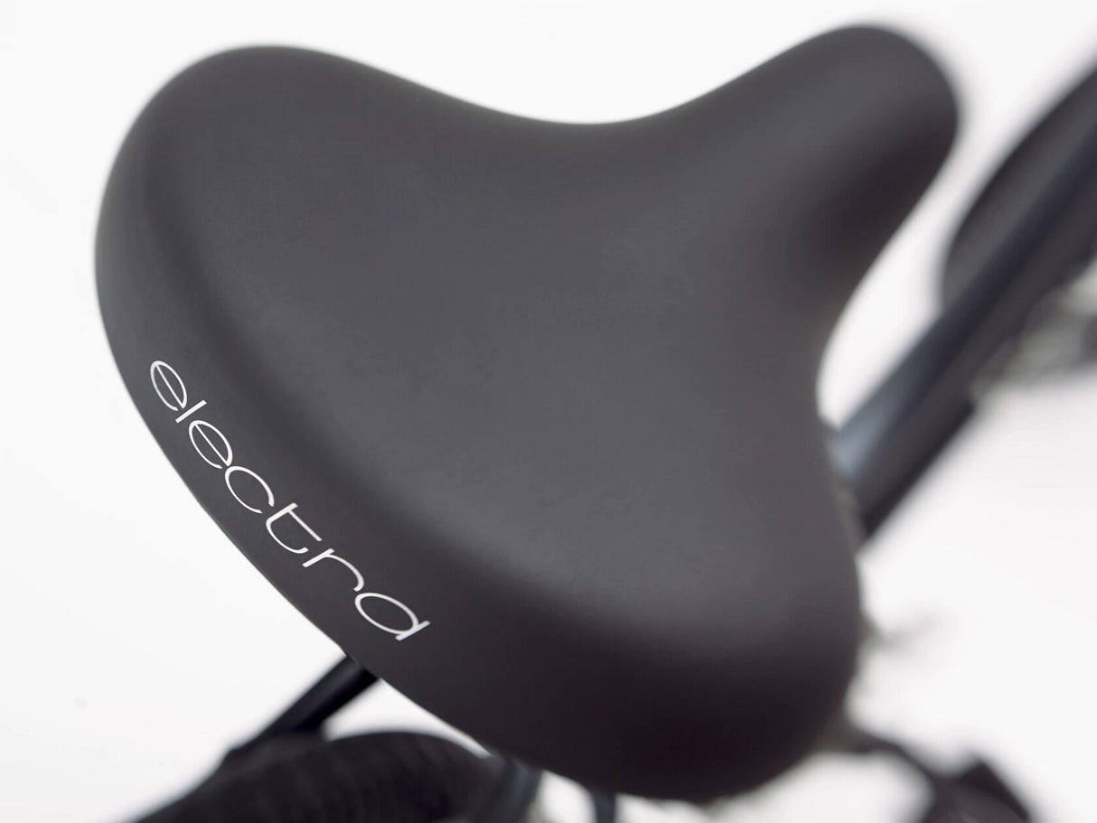 Close-up of a black bicycle seat with 'electra' branding on a blurred background