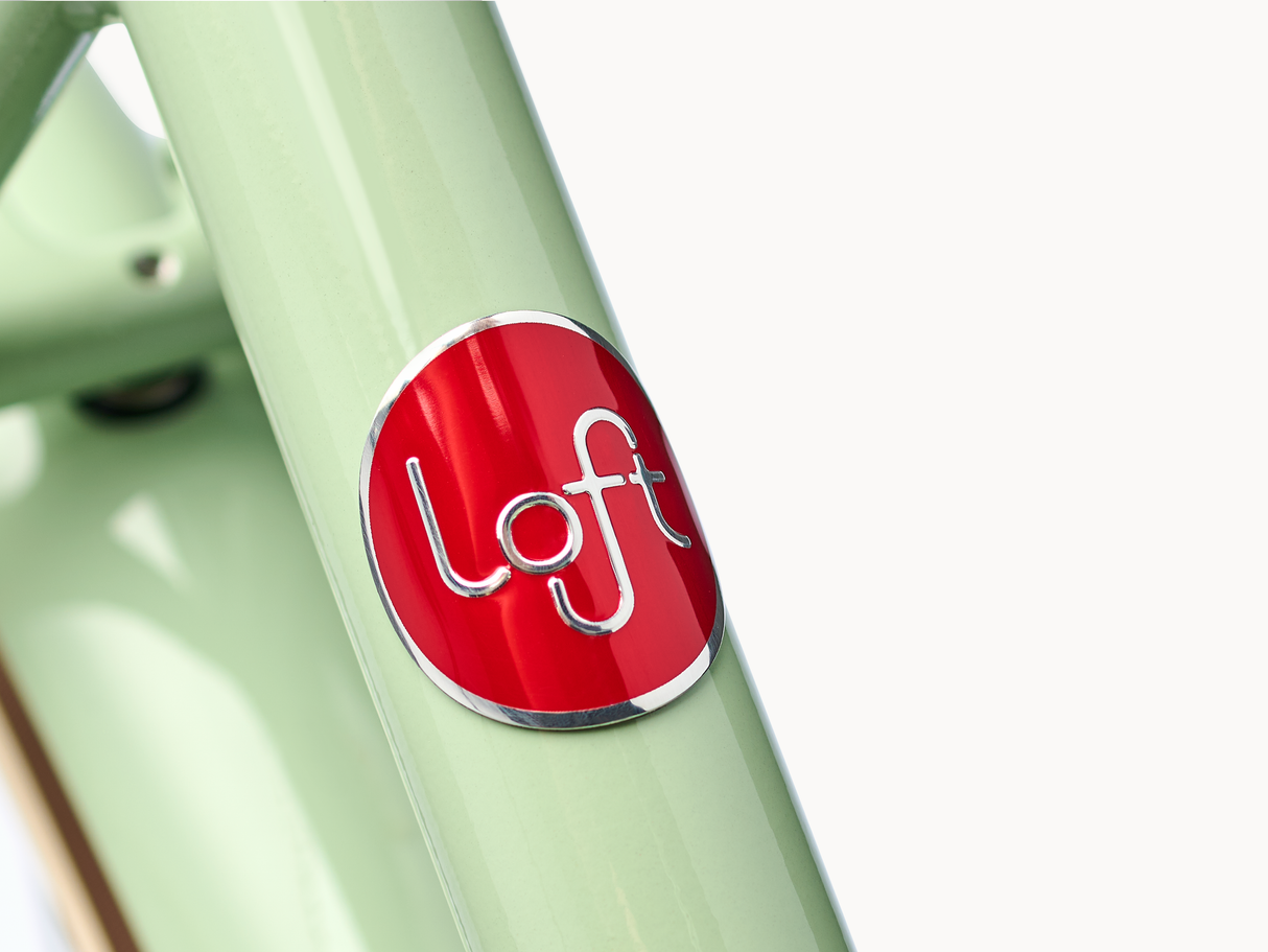 Close-up of a light green bicycle frame with a red 'loft' logo on a white background
