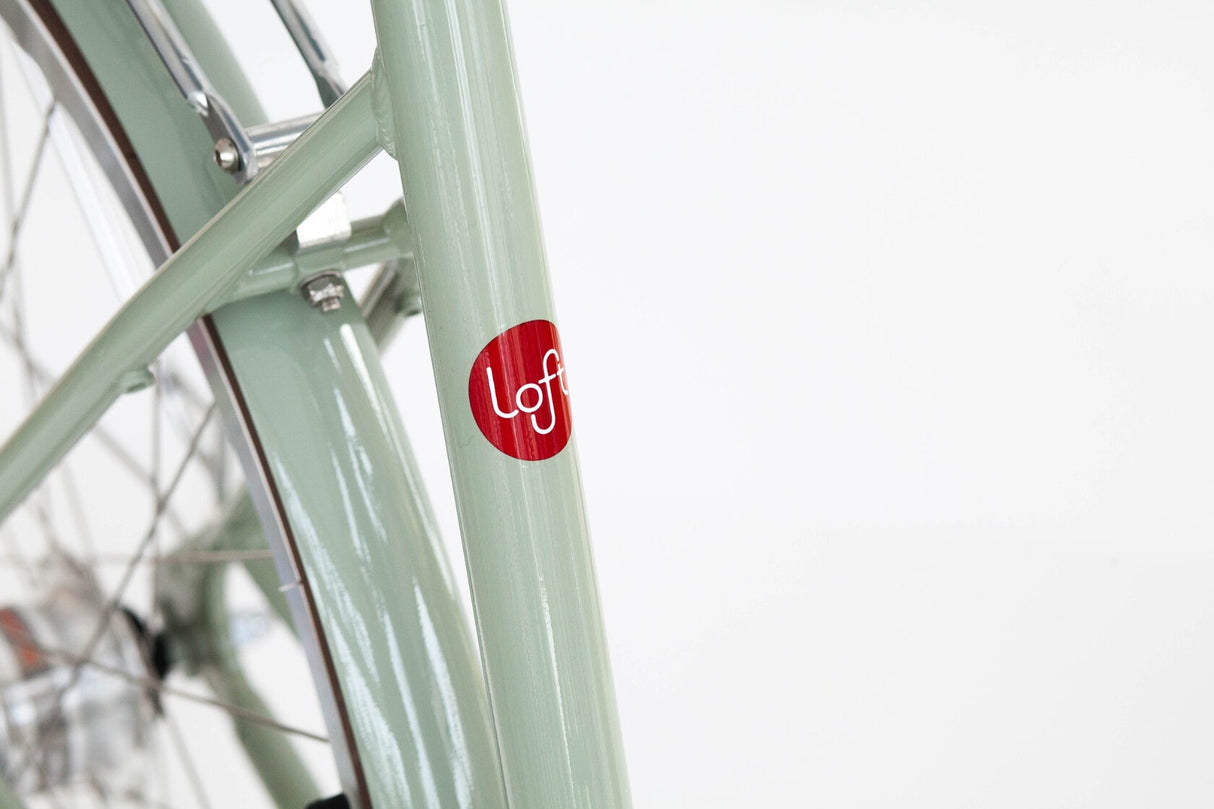 Close-up of a bicycle frame with a red 'loft' logo on a white background