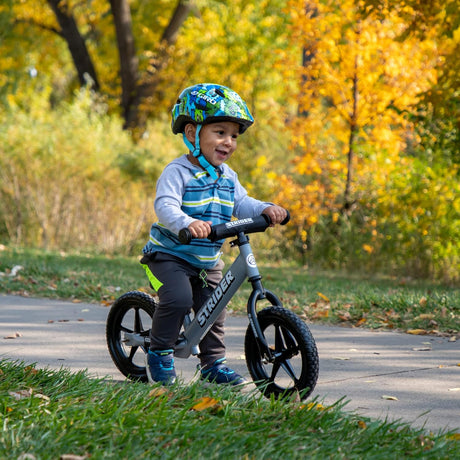 Child riding a balance bike in a park with autumn leaves